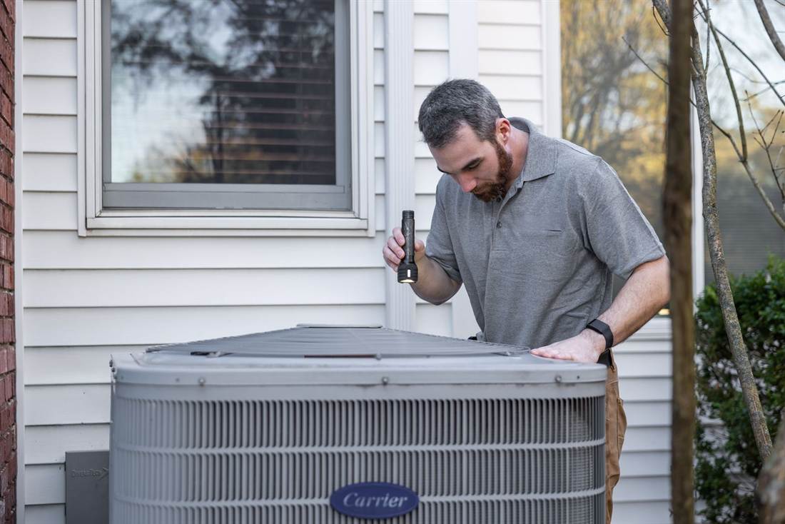 A technician servicing an outdoor air-conditioning condenser beside a house